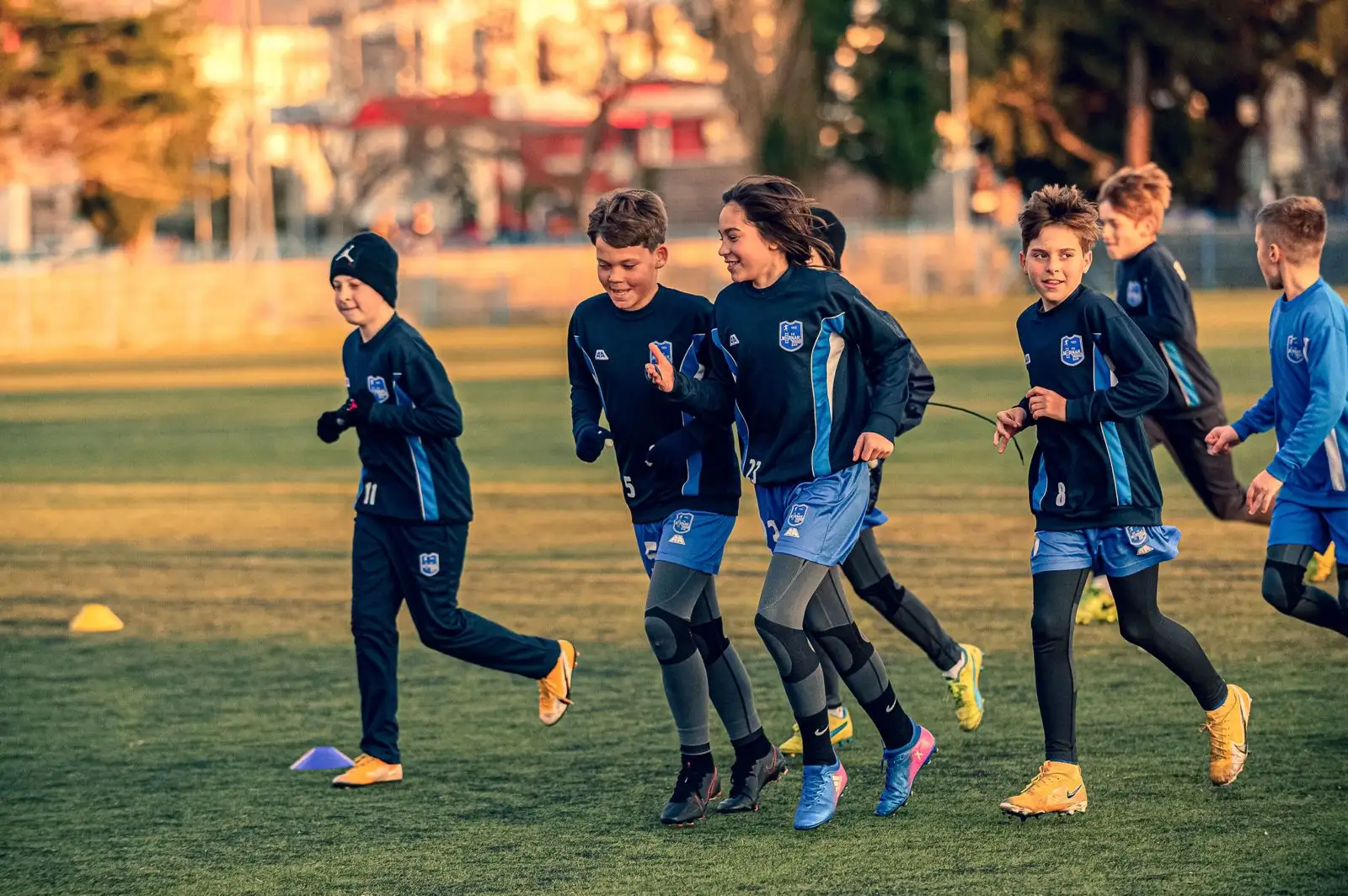 Jóvenes deportistas haciendo ejercicios con conos en un entrenamiento de fútbol con la luz de la mañana.